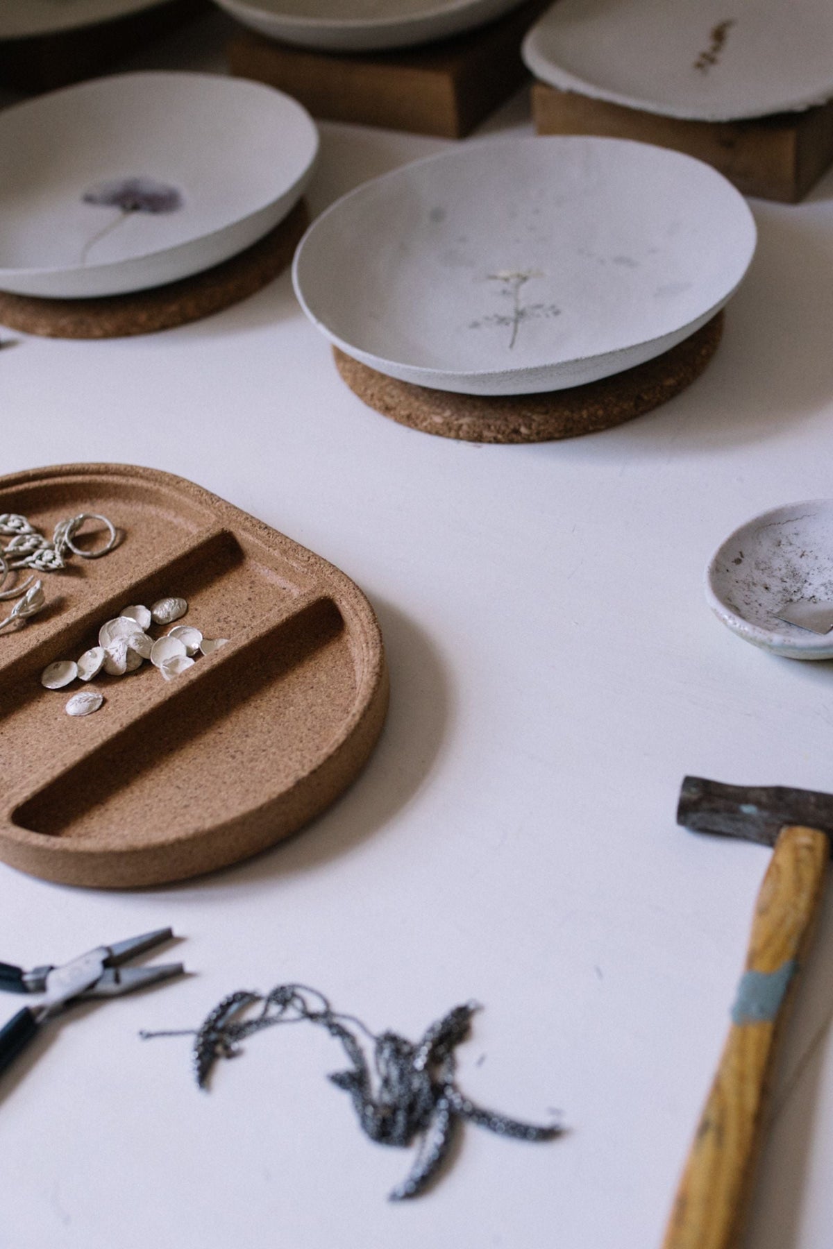 Mesa de trabajo con bandejas de cerámica, piezas de plata y herramientas de joyería
